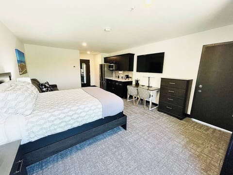 A bright, open room featuring a comfortable bed, work desk, ample storage, and a large TV, perfect for relaxing or working during your stay.