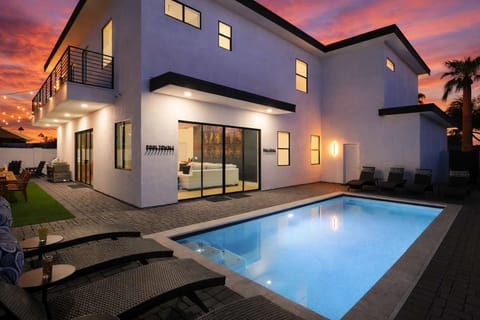 Resort-style backyard with a sparkling pool, sun loungers, an outdoor dining table for 12, a grill, and a cozy fire pit with surrounding seating.