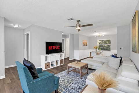 Modern living room with a white sectional sofa, blue armchair, and a television with streaming service access.