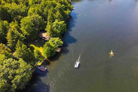 A scenic aerial shot reveals the home’s secluded lakeside location, with a private dock nestled among dense trees and boats enjoying the water.