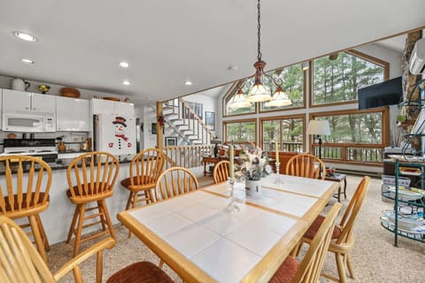 Comfortable dining space with a large table for six, surrounded by windows offering wooded views and natural light.