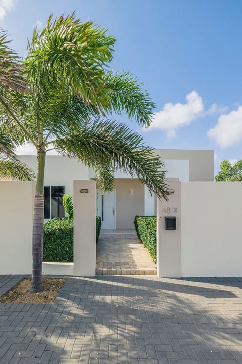 Modern tropical property entrance with palm trees, manicured hedges, and paver walkway leading through secure white-walled façade. Your vacation retreat awaits just beyond this welcoming arrival point.