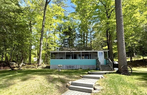 A charming turquoise cottage nestled in a lush, tranquil forest, offering a peaceful woodland retreat just steps away from Webster Lake.