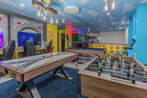 Experience our lively game room featuring a chic foosball table and air hockey table, all set against cheerful blue and yellow walls. The playful decor and cloud-patterned ceiling create a fun, relaxing atmosphere for everyone.
