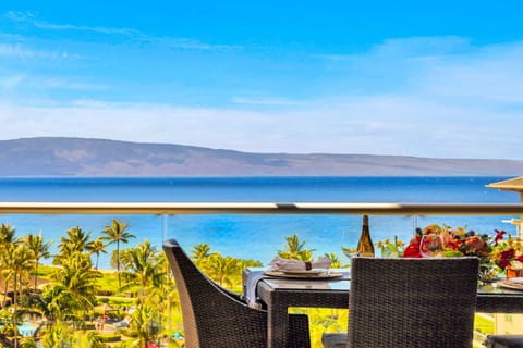 Elevated ocean view stretches over lush palms and rooftops to the sparkling blue beyond.