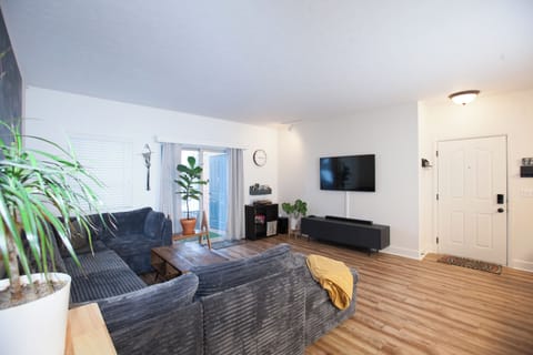 View of the living room, entertainment center, and sliding door that takes you to the balcony. The balcony has a gas grill, turf rug, and a small group of seating.