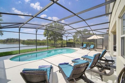 Beautiful sunny pool deck with a covered lanai and dining area, sun loungers, and a serene lake view.