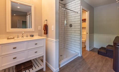 White vanity with silver fixtures stands beside a tiled walk-in shower and wood-look vinyl flooring.