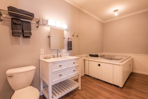 Bathroom features a white vanity with marble countertop and an in-room hot tub beside wood laminate flooring.
