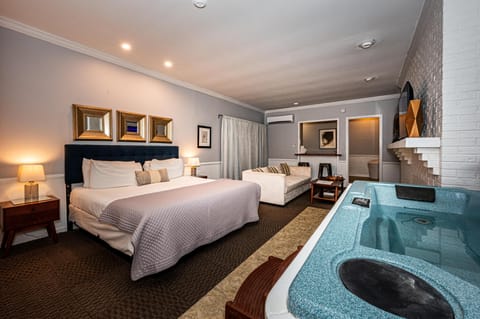 In-room hot tub with a blue granite finish beside a white sofa and king bed with navy headboard and gold-framed mirrors.