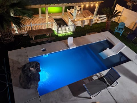 Rectangular pool illuminated with blue light, featuring a rock waterfall and a pool lift chair on the concrete deck.