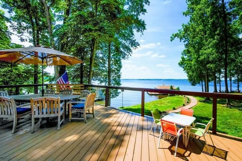 Lakefront deck with ample seating, a dining area under an umbrella, and breathtaking views of the water and surrounding trees.