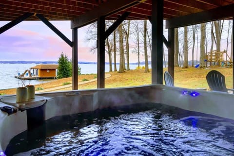 This serene view from the hot tub under the deck showcases the ultimate relaxation experience, overlooking the lake, boat dock, and fire pit area. Perfect for unwinding while soaking in the peaceful surroundings.