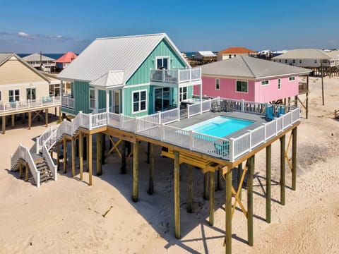 Coastal vacation rental featuring elevated design with private pool and sandy beachfront location among colorful neighboring properties.