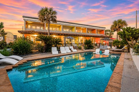 Oceanfront Galveston condo with resort-style pool, palm trees, lounge chairs, and colorful Seawall exterior views at sunset.