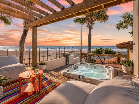 Sunset hot tub lounge featuring ocean views, pergola-covered seating, and a cozy beachfront setting for evening relaxation.