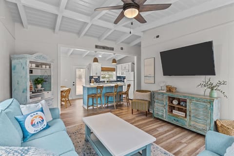 Cozy Oak Island NC living room featuring blue sofas, wall-mounted TV, coastal console cabinet, ceiling fan, and bright windows creating a relaxed beach cottage atmosphere