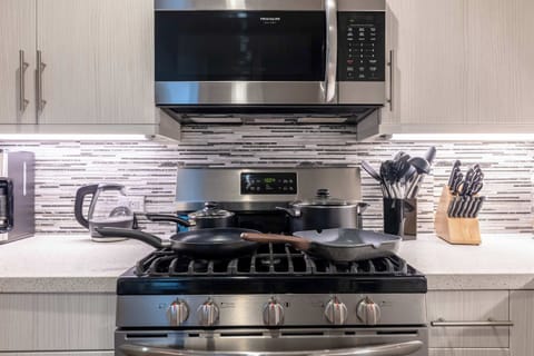A sleek stainless-steel gas range and microwave framed by a glossy mosaic backsplash — modern elegance meets functionality.
