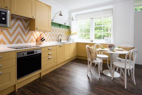 Grooms Cottage - a pop of yellow in the dining area and well-equipped kitchen with electric oven and induction hob, fridge/freeze, dishwasher, and microwave
