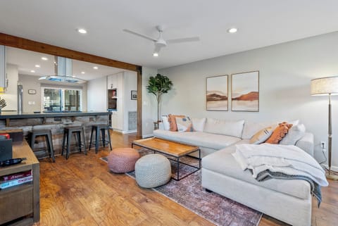 Relax in this stylish open living space, featuring a plush white sectional and warm wooden accents. The inviting layout includes a rustic breakfast bar and cosy pouffes, creating the perfect spot to relax after a day of exploring.
