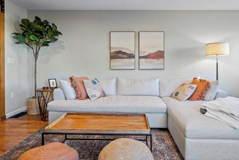 Relax in this bright, modern living room featuring a plush white sectional and a warm wooden coffee table. Accented with abstract art and a vibrant fiddle-leaf fig, this serene space is the perfect spot for quiet downtime.