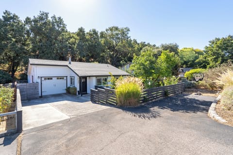 This charming cottage includes a spacious paved driveway, a private garage, and even a basketball hoop for outdoor fun, all tucked away against a beautiful backdrop of mature trees.