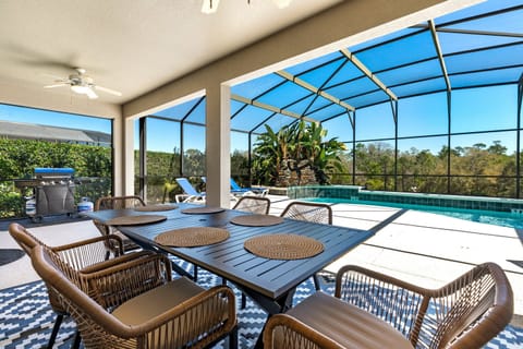 This covered outdoor space features a large dining table with seating for six, stylish wicker chairs, a ceiling fan for added comfort, and direct views of the screened-in pool, and spa.