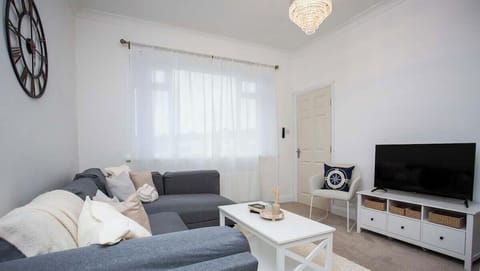Relax in this bright, cozy living room featuring a comfy sectional sofa, soft neutral decor, and a flat-screen TV. The large window lets in plenty of natural light, creating a warm and inviting atmosphere.