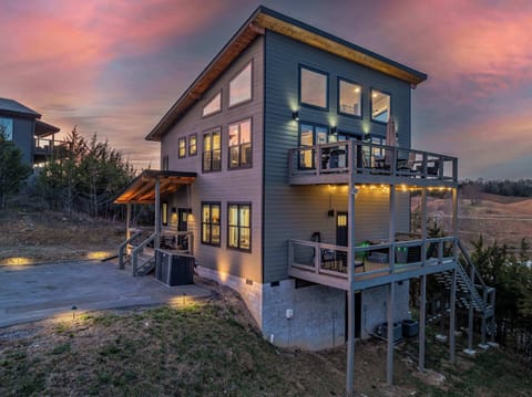 The mountain home exterior shines at sunset, with warm lighting that highlights the architecture and creates a welcoming glow against the scenic backdrop.