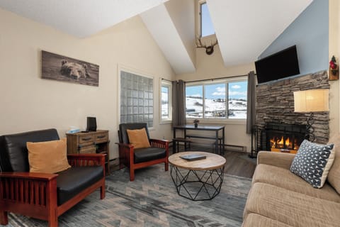 Cozy up by your stone fireplace at Summit Unit 1303 while gazing at snowy mountain views through expansive windows in this inviting alpine retreat.