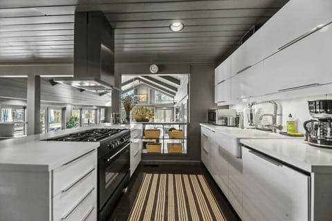 Modern kitchen with sleek white cabinetry, dishwasher,  stainless steel appliances, and a bold striped runner adding warmth and texture.