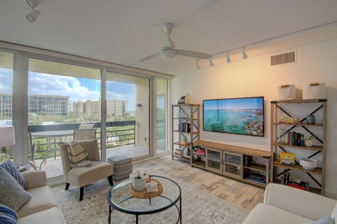 Living room with glass sliding doors opening to a balcony, light wood flooring, and a wall-mounted flat-screen TV.