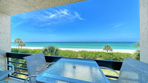 Balcony with glass-top table and mesh chairs overlooks palm trees, white sand beach, and turquoise Gulf waters.
