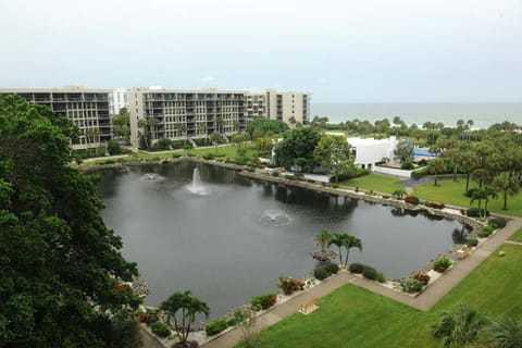 View from balcony overlooks a large fountain pond, manicured lawns, and palm trees with the Gulf beyond.