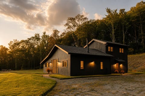 Arrive to this modern barn-style home glowing at dusk, tucked right against the treeline. The open lawn and gravel drive give you space to unload and settle in for the night.