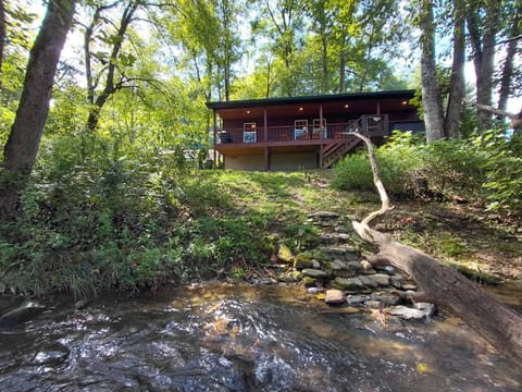 Exterior view of the Creekside Too cabin positioned above a wooded creek bank in Bryson City, NC. The secluded setting highlights the natural surroundings and creekside location near the Smoky Mountains.
