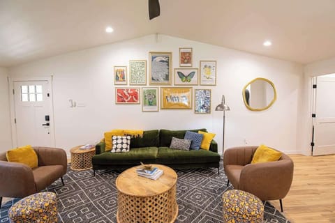 Relax in this vibrant, eclectic living room featuring a plush olive green velvet sofa, brown accent armchairs, patterned poufs, and an eye-catching gallery wall display above a patterned area rug.