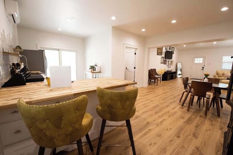 Enjoy an open-concept layout featuring a wooden kitchen island with stylish yellow barstools, light wood flooring, and a seamless flow into the dining and living spaces.