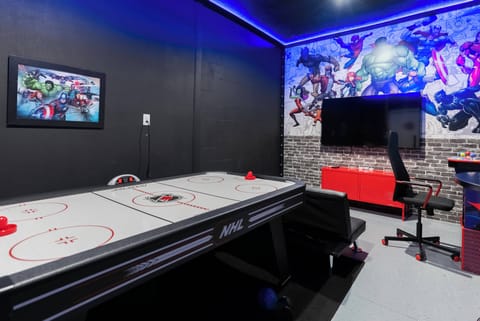 Step into a vibrant game room featuring a sleek air hockey table that promises hours of fun. Striking blue LED lighting enhances the playful atmosphere, while the bold mural adds a dynamic touch to this engaging space.