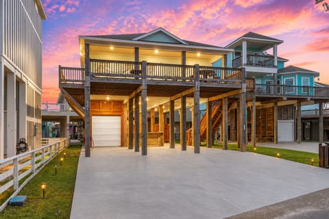 Elevated Bolivar Peninsula vacation home with a spacious covered front deck, wide concrete driveway, wood pilings and coastal architecture.