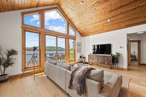 Unwind in your lakefront living room where warm wood ceilings meet panoramic windows, creating the perfect space to relax with nature's tranquil views.
