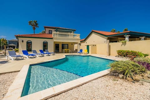 A vibrant vacation home with a sparkling pool surrounded by lush greenery, perfect for unwinding under the clear blue skies in complete relaxation.