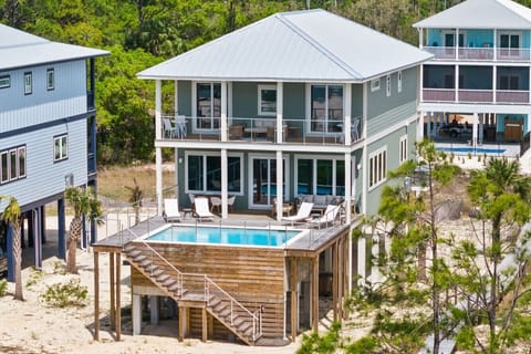 Elevated beach house with private pool surrounded by coastal palms and neighboring vacation homes.