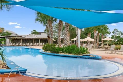 Relax under vibrant blue shade sails by the sparkling pool, surrounded by swaying palms and tropical landscaping. Lounge chairs and shaded seating areas invite you to unwind poolside in paradise.