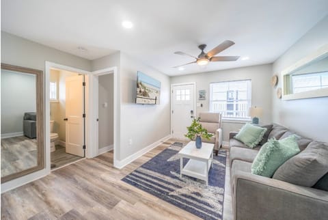 Spacious open living area with smart TV, cozy sofa, and modern coastal decor. Bright lighting, ceiling fan, and easy access to bathroom and entry make this a comfortable space to relax after the beach.