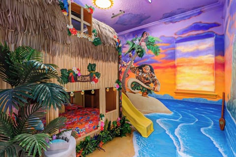 Magical Moana-themed hideaway with custom tiki hut bunk bed and yellow slide. Immersive hand-painted sunset murals transform walls into tropical paradise. Thatched roof details, palm trees, and island decor create Disney-inspired adventure space.