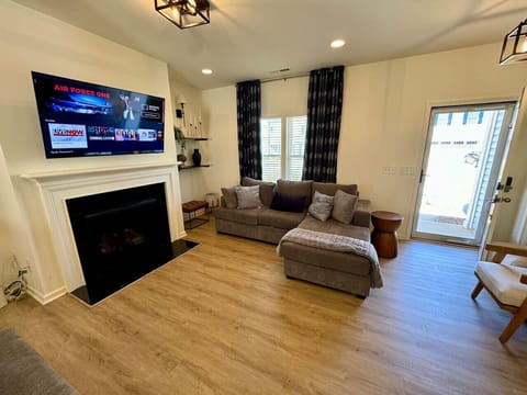 Modern living room with a sectional sofa, fireplace, mounted TV, floating shelves, and patio access.