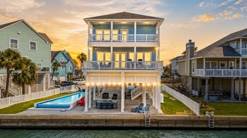 Canal-front Galveston vacation home at sunset with a private swimming pool, spacious covered decks, outdoor seating and panoramic waterfront views.