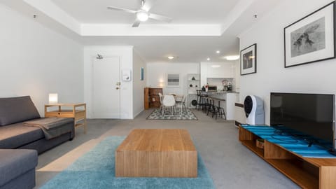 Bright open plan living area featuring comfortable seating, a TV and large windows that fill the space with natural light.