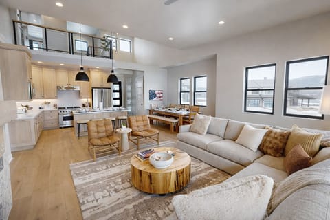 Relax in your spacious open-concept haven where natural light floods through expansive windows, highlighting the warm wood accents and plush sectional sofa perfect for gathering.